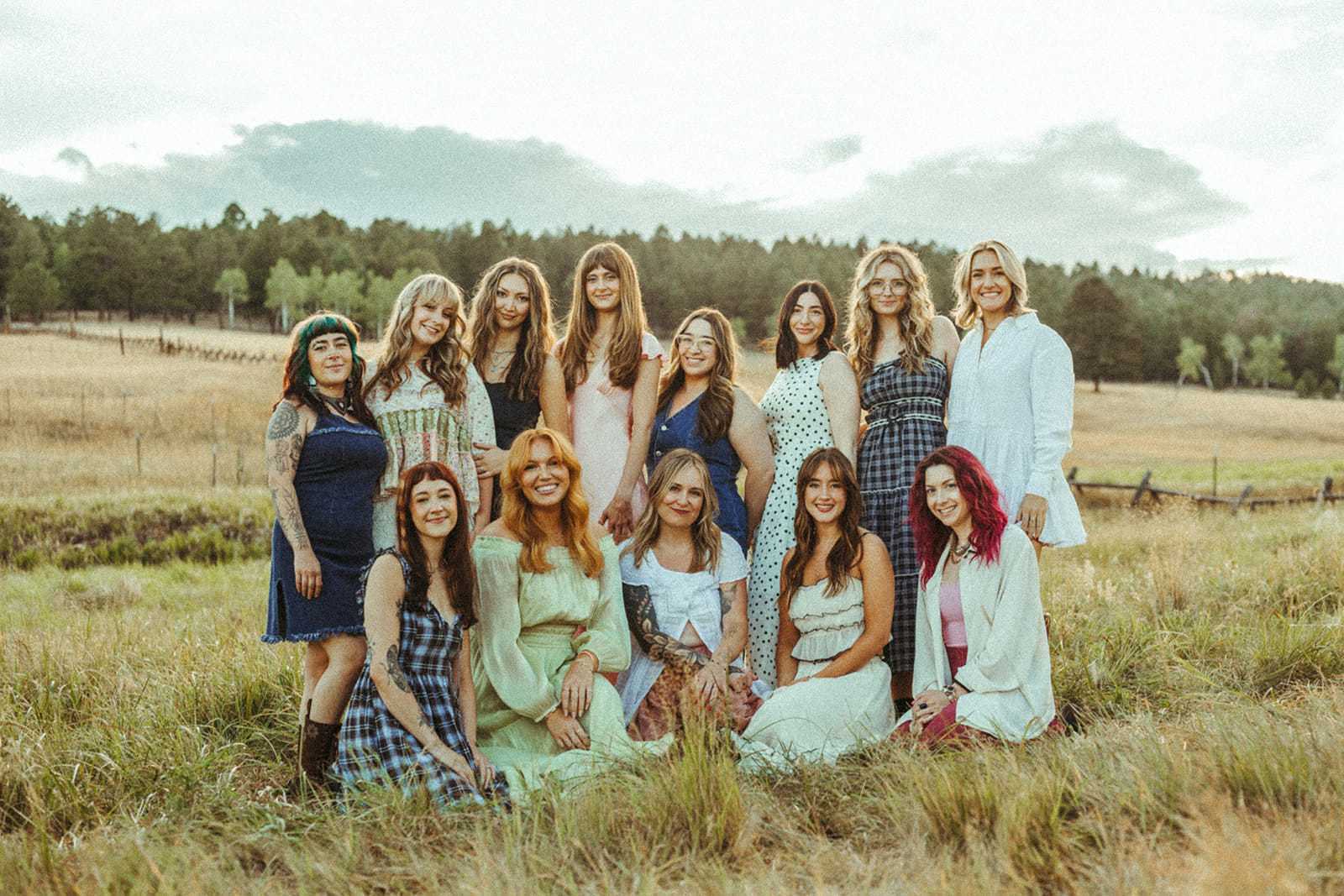Group of women smiling outdoors in a grassy field, trees in the background.