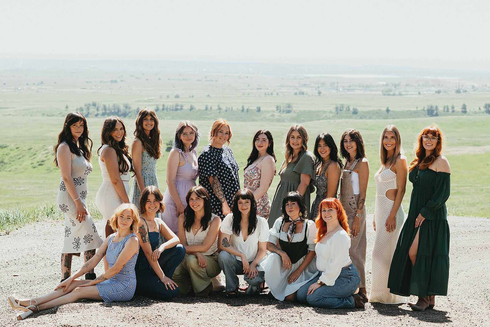 A group of diverse women pose together outdoors with a scenic landscape in the background.